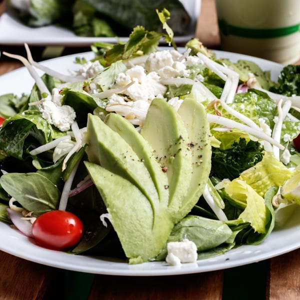 A vibrant Nokturne World Kitchen & Juice salad with avocado, feta, cherry tomato, and greens.