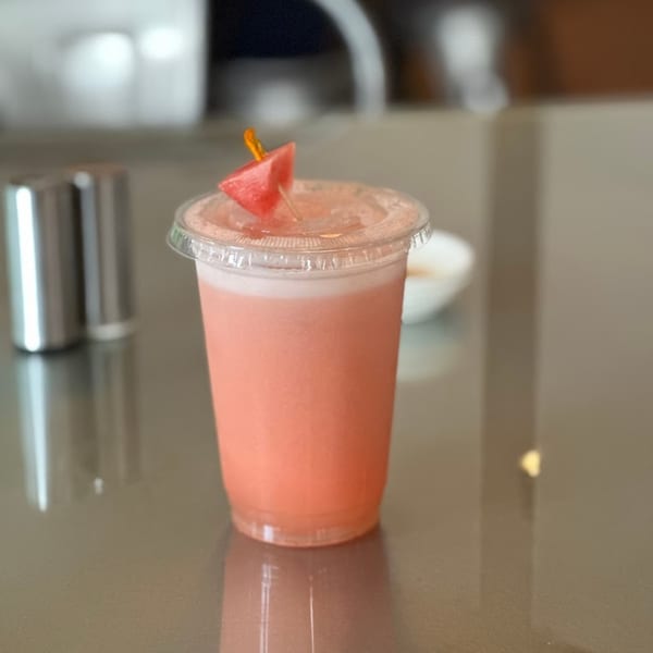 A pink watermelon juice with a watermelon slice garnish sits on a reflective table.