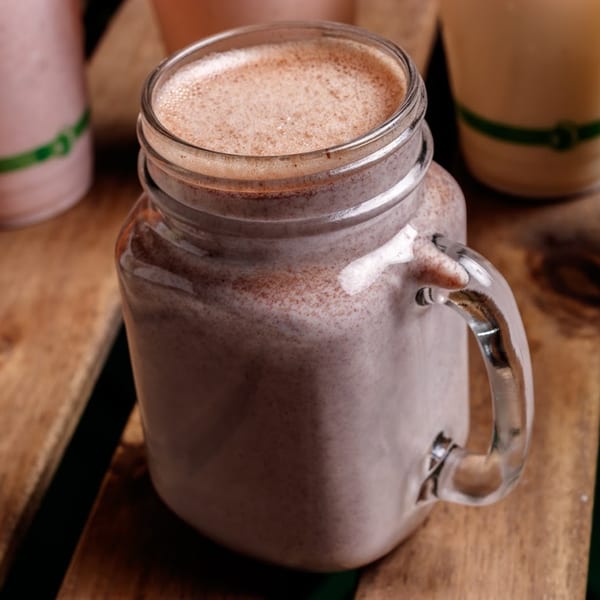 A healthy smoothie in a glass jar with a handle, on a rustic wooden surface.