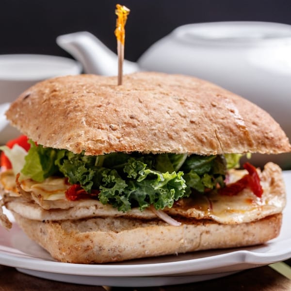 A healthy Nokturne World Kitchen sandwich with chicken, kale, and red peppers on a whole-grain bun.