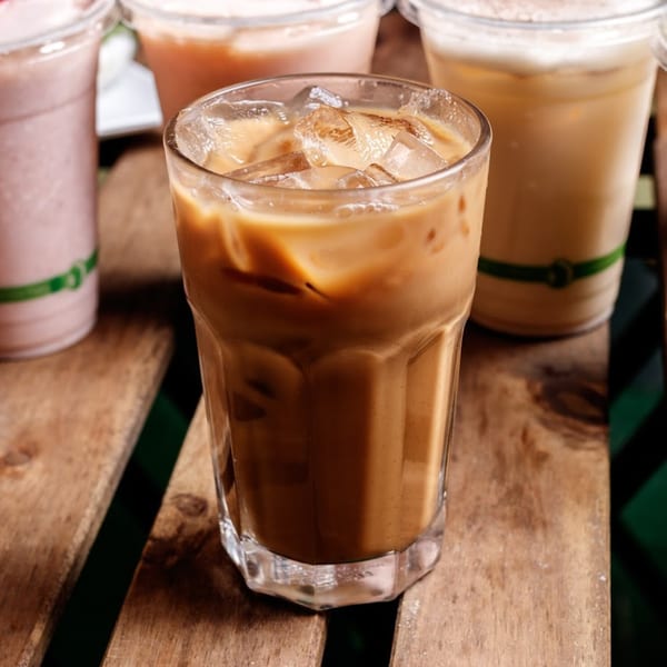 Iced coffee in a glass with other drinks in the background on a wooden table.