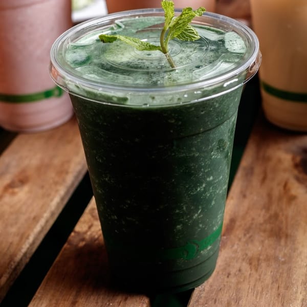 A vibrant green smoothie with a mint garnish in a clear cup on a rustic wooden surface.