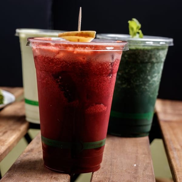 Three healthy juices in clear cups on a wooden surface, with a red juice in the foreground.