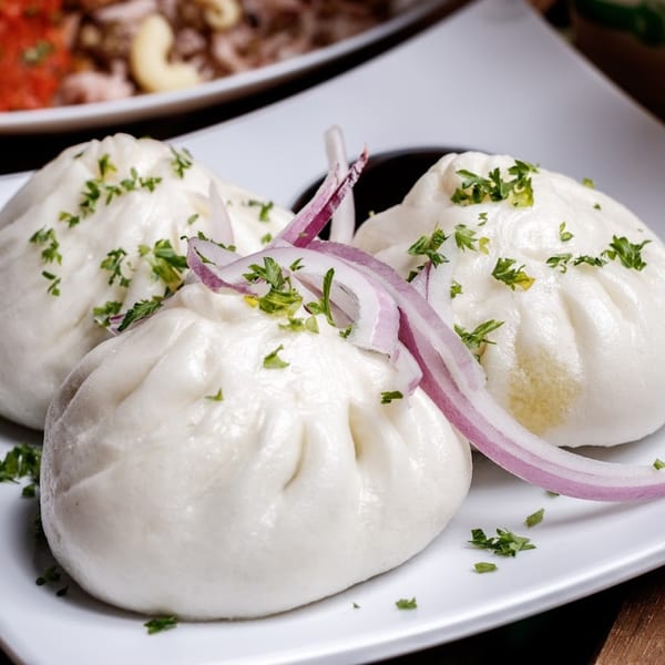 Three steamed buns topped with red onion slices and fresh parsley on a white plate.